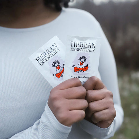 Person holding Herban Essentials yoga wipes in a natural setting