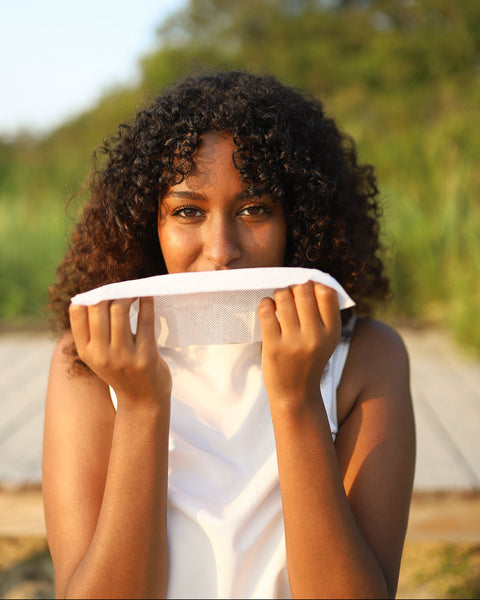 Woman holding a herban essentials  essential oil towelette  over her face with a blurred natural background