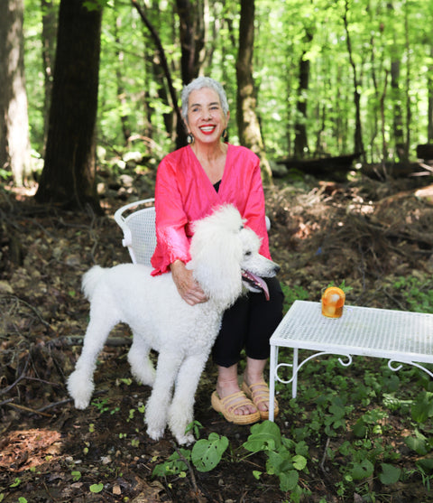 Herban Essentials founder with a white poodle, seated in a sunlit forest