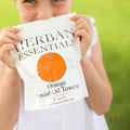 Child holding a Herban Essentials Orange Essential Oil Towelette against a grassy background