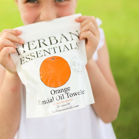 Child holding a Herban Essentials Orange Essential Oil Towelette against a grassy background