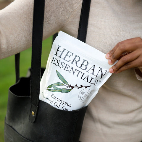 Person holding a black tote bag with 'Herban Essentials' product