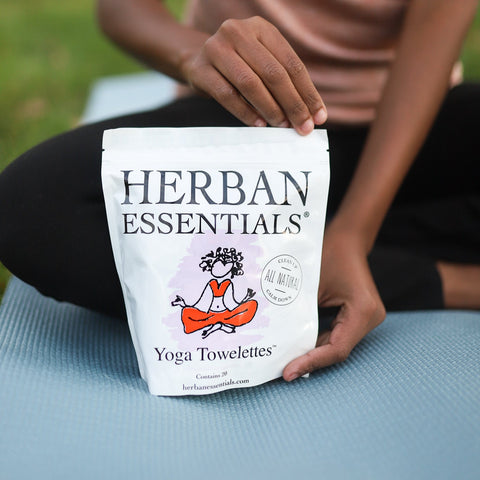 Person holding a Herban Essentials yoga towellettes package on yoga mat.
