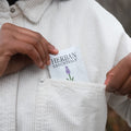 Person holding a 'Herbary Essentials' towelette in a white corduroy jacket pocket