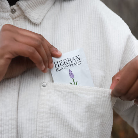 Person holding a 'Herbary Essentials' towelette in a white corduroy jacket pocket