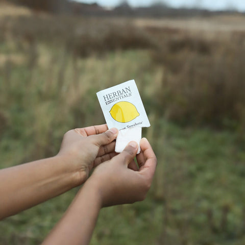 Person taking out a herban essentials lemon essential oil wipe with a blurred field background