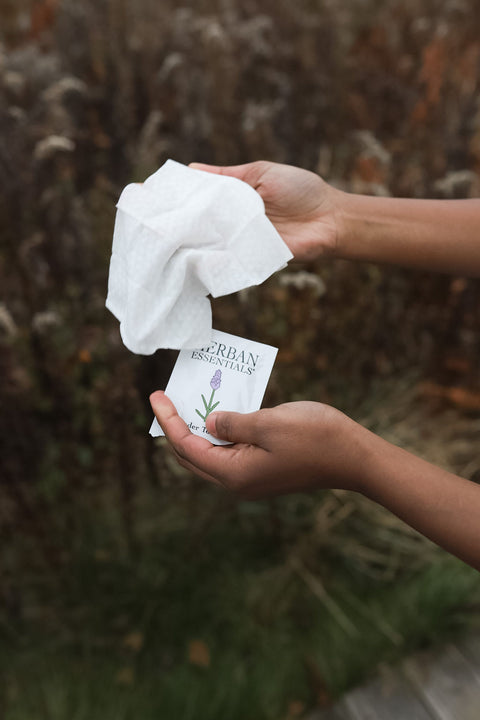 Hand opening a Lavender Essential Oil Towelette single packet outdoors.