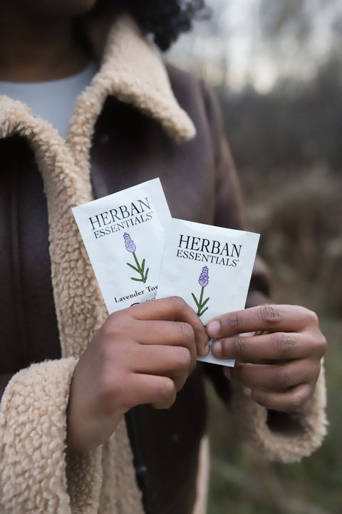 woman in brown coat holding two herban essentials individually wrapped wipes. 